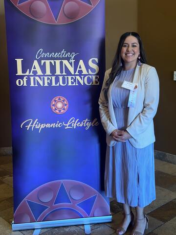 Arlene Cano Matute standing by Latina of Influence Award banner.
