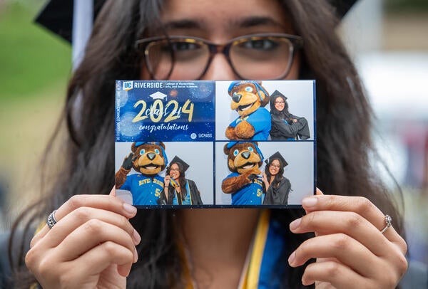 Graduate holding up photo of themself with UCR's mascot Scotty the Bear