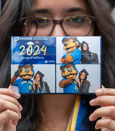 Graduate holding up photo of themself with UCR's mascot Scotty the Bear