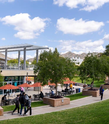 UCR campus: modern building, outdoor seating, green lawn, students, distant hills.