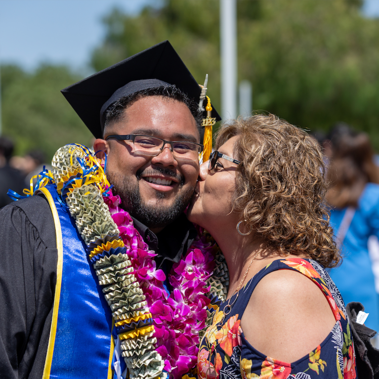 Graduate being kissed on cheek by family member.