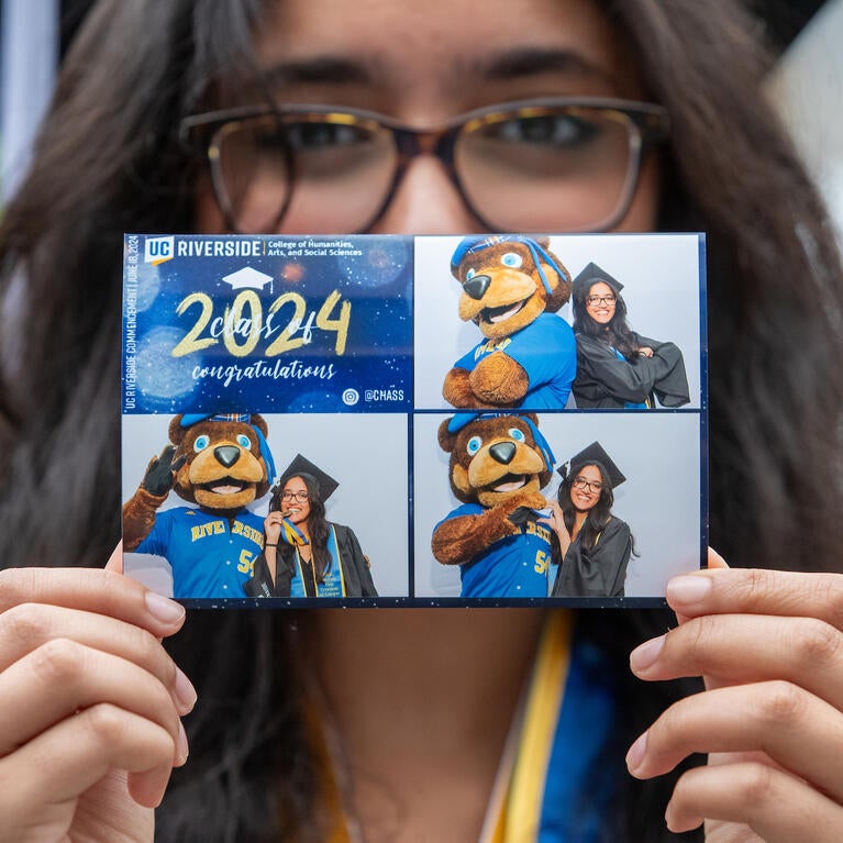 Graduate holding up photo of themself with UCR's mascot Scotty the Bear