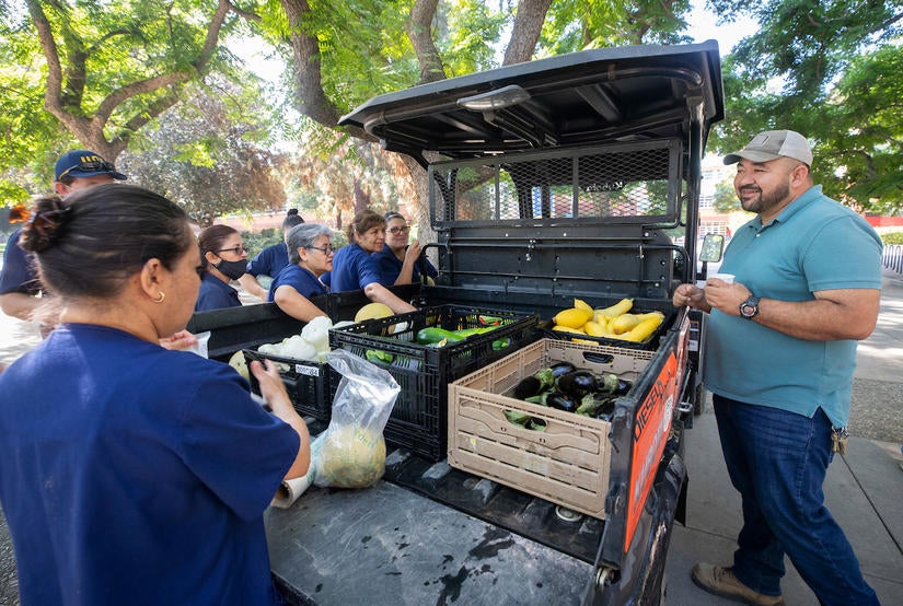 Richard Zapien, R’Garden manager (right) drove to the coffee social on Tuesday, July 27, with vegetables and cantaloupe to share with faculty and staff members. (UCR/Stan Lim)